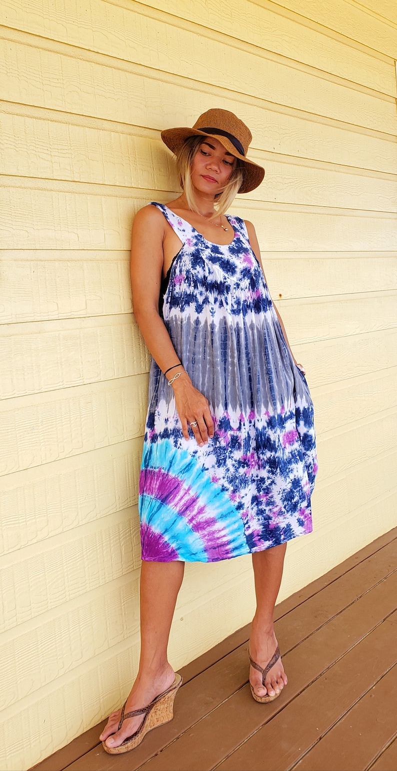 May include: A woman wearing a tie-dye maxi dress with a brown hat and brown wedge sandals. The dress has shades of blue, purple, and white.