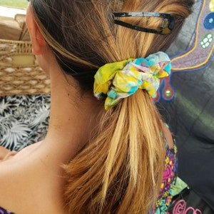May include: A woman with long, blonde hair pulled back in a ponytail with a colorful scrunchie and a black barrette.