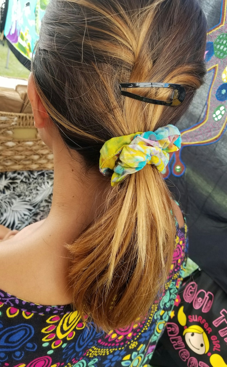 May include: A woman with long, blonde hair pulled back in a ponytail with a colorful scrunchie and a black barrette.
