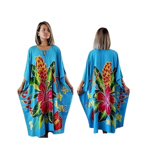 May include: A blue, floral print kaftan with a tie at the neck. The print features a large hibiscus flower, a ginger flower, and green leaves.