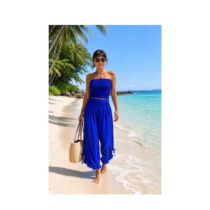 May include: A vibrant royal blue two-piece set consisting of a strapless, smocked tube top and matching wide-leg trousers with a high, elasticized waistband and ruffled hem details, paired with a woven straw tote bag and dark sunglasses.
