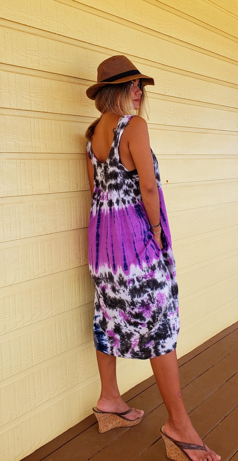 K&ouml;nnte beinhalten: Eine Frau tr&auml;gt ein lila, schwarz und wei&szlig;es tie-dye-Kleid ohne &Auml;rmel mit einem braunen Hut und braunen Keilsandalen.