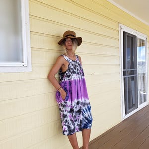 K&ouml;nnte beinhalten: Eine Frau tr&auml;gt ein lila, blaues und wei&szlig;es Batik-Kleid mit einem braunen Hut und braunen Keilsandalen.
