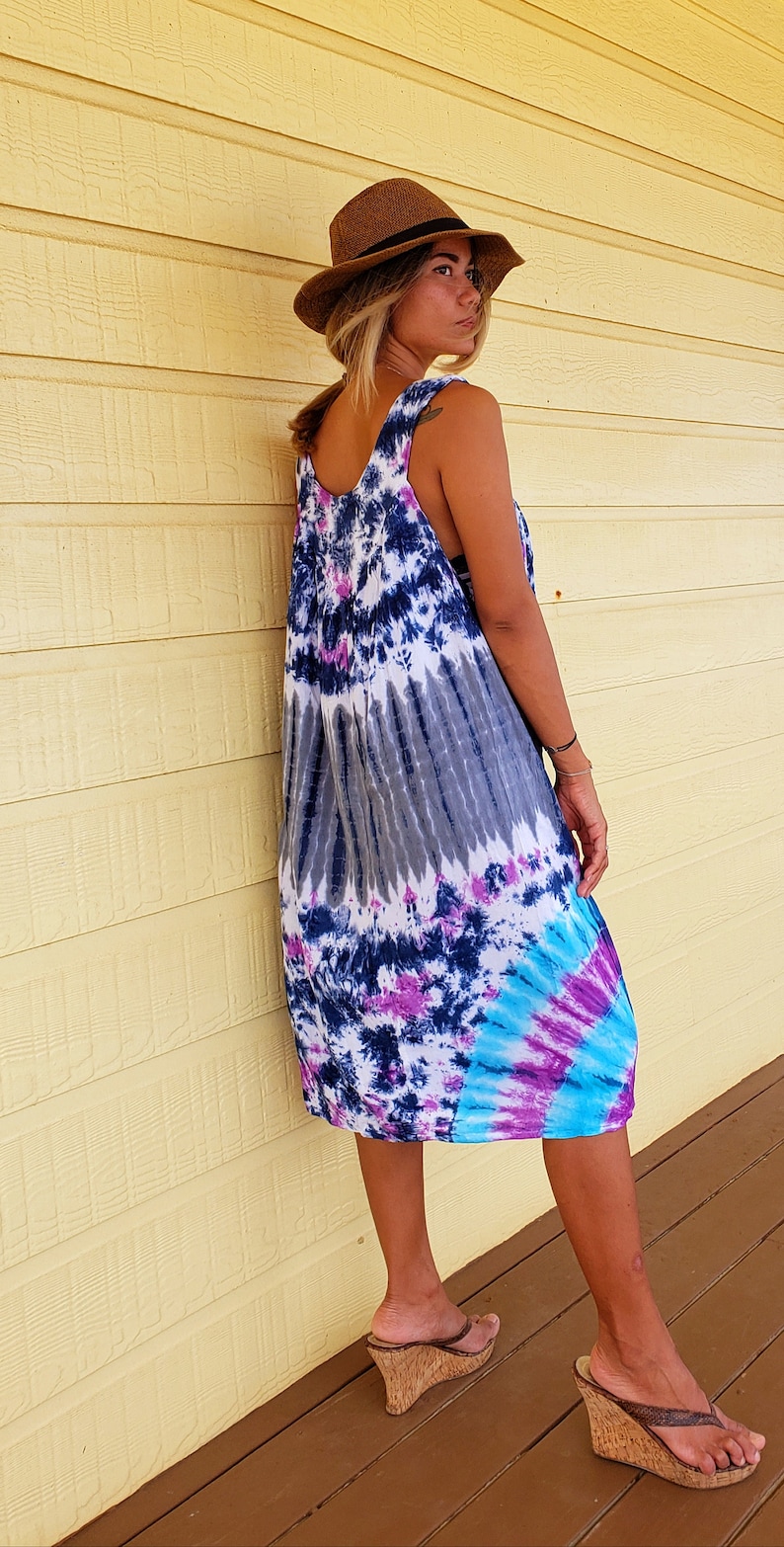 May include: A woman wearing a tie-dye maxi dress with a brown hat and brown wedge sandals. The dress has shades of blue, purple, and white.