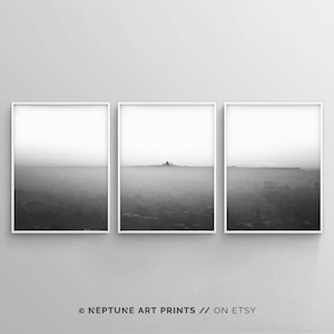 May include: A set of three black and white landscape photographs in white frames. The photographs depict a hazy, distant cityscape.