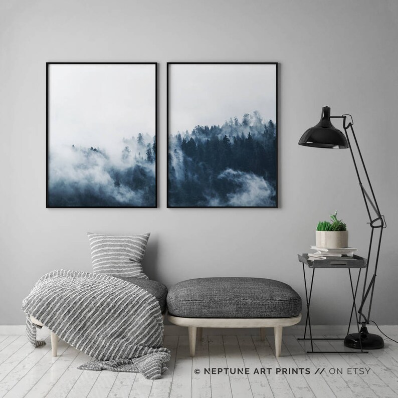 May include: Two framed prints of a misty forest scene in shades of blue. The prints are hung on a gray wall above a gray ottoman with a striped throw blanket.