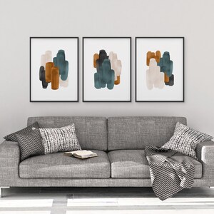 May include: Three framed abstract art prints with a gray background. The prints feature overlapping shapes in shades of teal, brown, and beige.