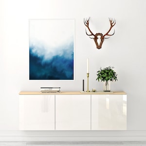 May include: White cabinet with three doors, a wooden top, and a blue and white abstract painting hanging on the wall above it. A set of books and a small plant are on the top of the cabinet. A set of antlers is mounted on the wall to the right of the painting.