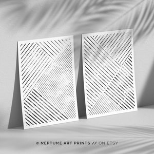 May include: Two black and white geometric line art prints with a distressed texture. The prints are on white paper and are leaning against a white wall.