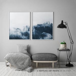 May include: Two framed prints of a misty forest scene in shades of blue. The prints are hung on a gray wall above a gray couch with a white and gray striped throw blanket.