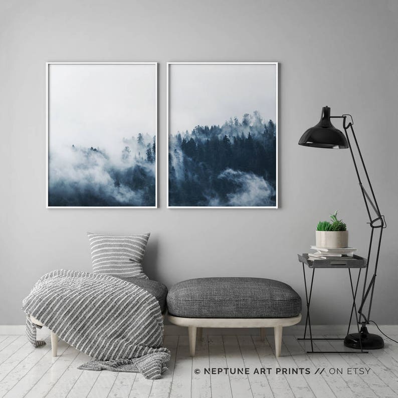 May include: Two framed prints of a misty forest scene in shades of blue. The prints are hung on a gray wall above a gray couch with a white and gray striped throw blanket.