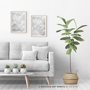 May include: Two black and white abstract geometric prints in wooden frames hang on a white wall above a gray sofa with a green plant in a woven basket.