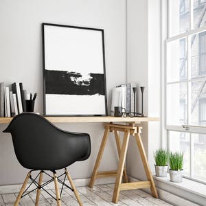 May include: A black and white abstract art print in a black frame hangs above a wooden desk with a black chair. The desk is supported by two wooden sawhorses. There are two potted plants on the floor next to the desk.