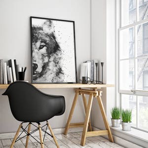 May include: Black and white watercolour painting of a wolf's face, framed and hanging on a white wall above a wooden desk with a black chair and plants.