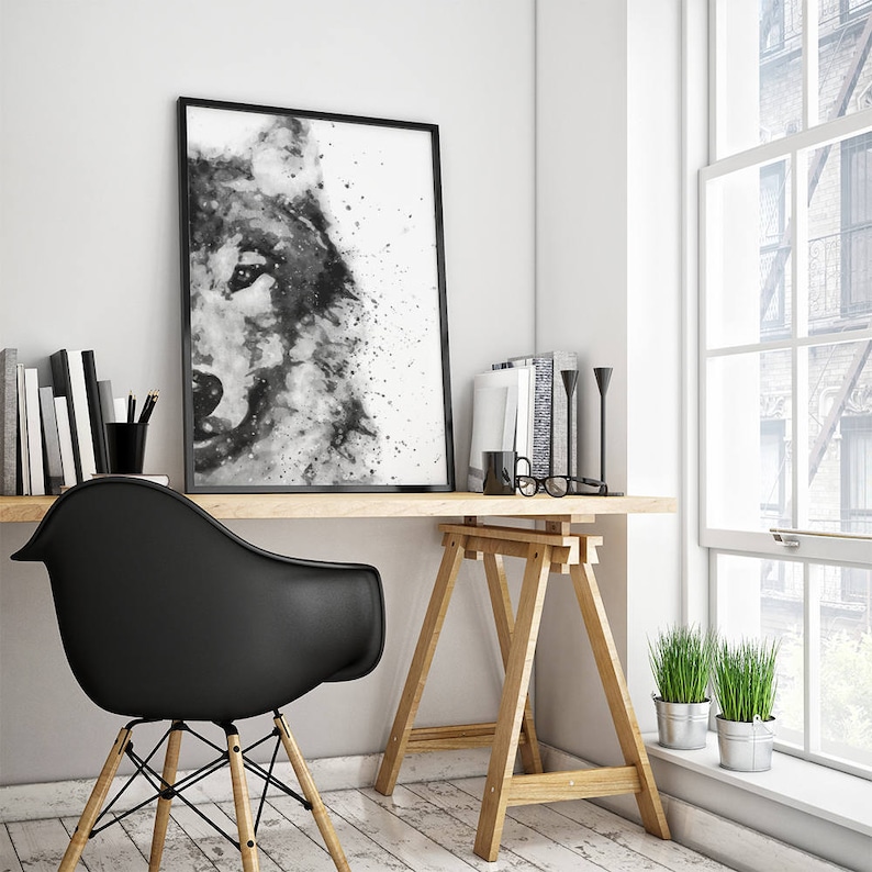 May include: Black and white watercolour painting of a wolf's face, framed and hanging on a white wall above a wooden desk with a black chair and plants.