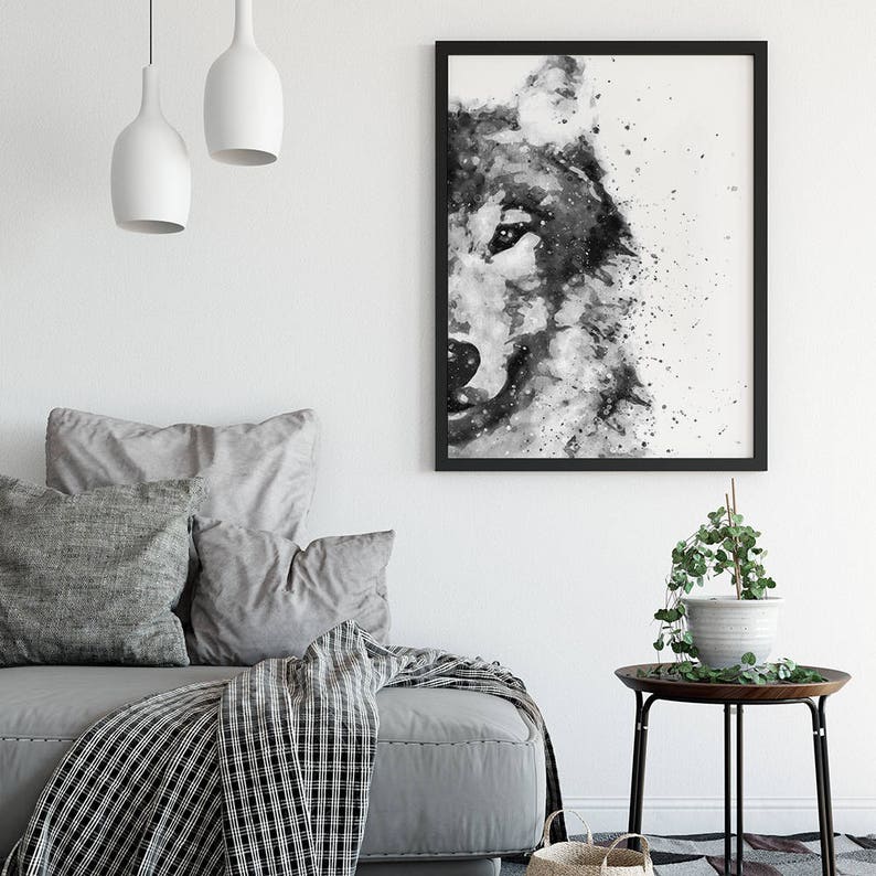 May include: Black and white watercolour painting of a wolf's face with a splatter effect. The painting is framed in a black frame and hanging on a white wall.