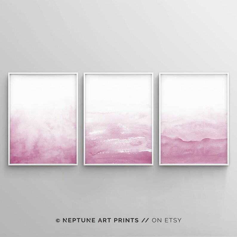 May include: Set of three abstract watercolor prints in shades of pink. The prints are framed in white and feature a gradient of pink from light to dark.