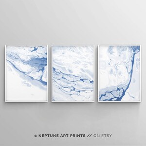 May include: Set of three abstract art prints featuring blue and white marbled designs. The prints are framed in white and displayed on a white wall.