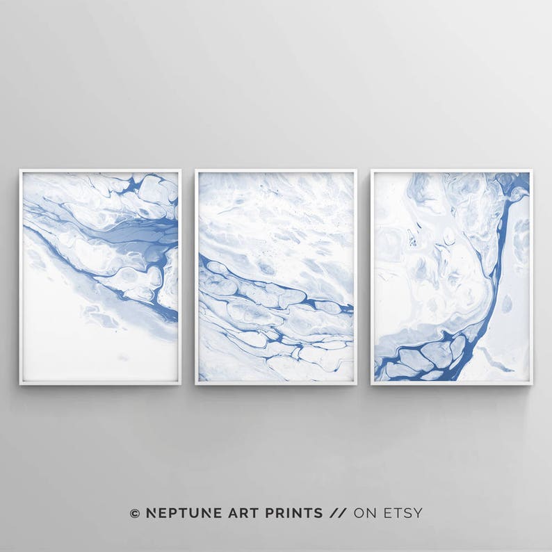 May include: Set of three abstract art prints featuring blue and white marbled designs. The prints are framed in white and displayed on a white wall.
