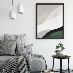 Puede incluir: Un sof&aacute; gris con almohadas y una manta de lana en blanco y negro. Una impresi&oacute;n abstracta enmarcada en negro con colores grises, blancos, verdes y negros cuelga de la pared sobre el sof&aacute;. Una peque&ntilde;a mesa auxiliar con una planta en maceta se encuentra junto al sof&aacute;.