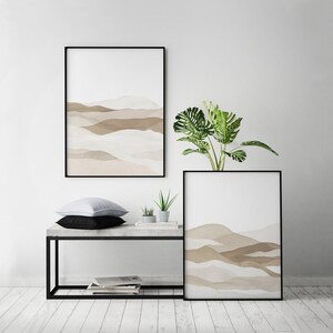 May include: Two framed abstract watercolor prints of brown and beige mountains with a green plant in a pot on a concrete shelf with a black metal frame.