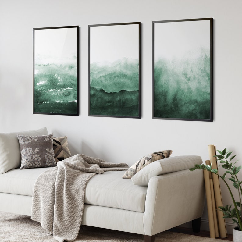 May include: Three framed abstract watercolour paintings with a green and white colour scheme. The paintings are hung on a white wall above a white sofa.