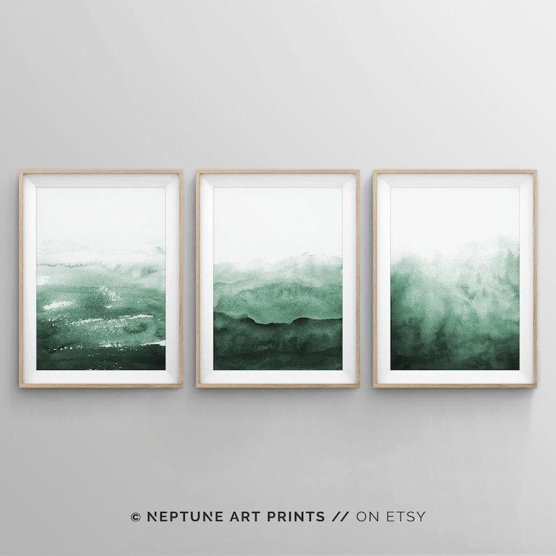 May include: Set of three framed abstract watercolour prints with a green and white colour scheme. The prints feature a layered, hazy, landscape design.