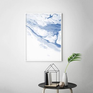 May include: Abstract art print with a white background and blue marbling. The print is framed in a white frame.