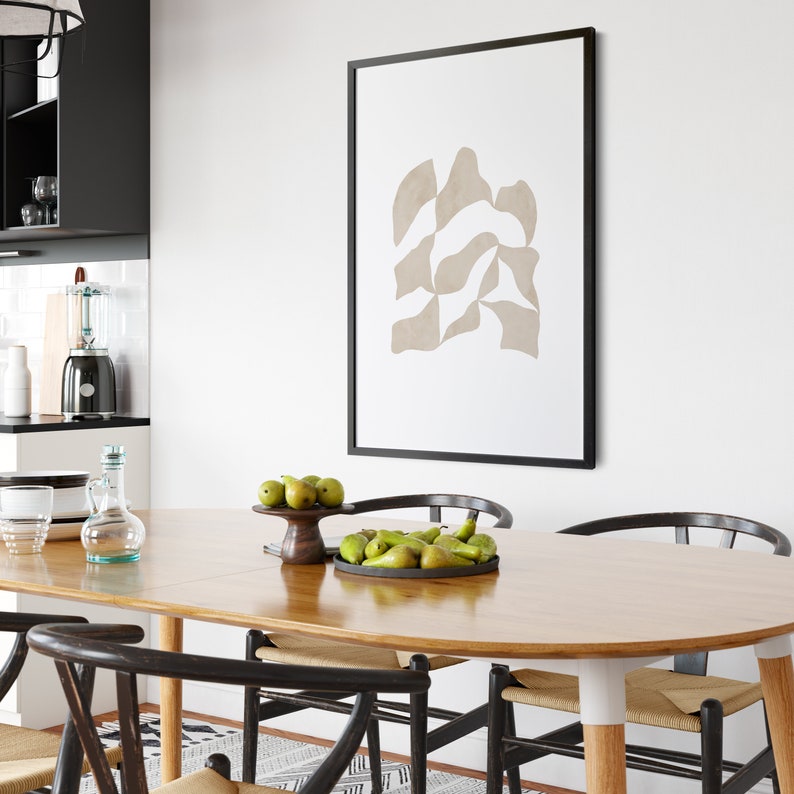 May include: A wooden dining table with a light wood finish and a black framed abstract art print on the wall behind it. The table is set with a bowl of green pears and a vase of clear glass.
