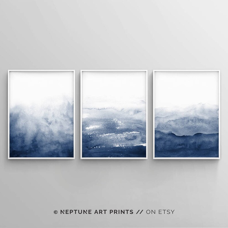 May include: Set of three abstract watercolour prints in shades of blue. The prints are framed in white frames and feature a gradient of blue from light to dark.
