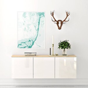 May include: White wall mounted cabinet with three doors. The cabinet has a light wood top and is decorated with a framed abstract painting, a set of antlers, and a potted plant.