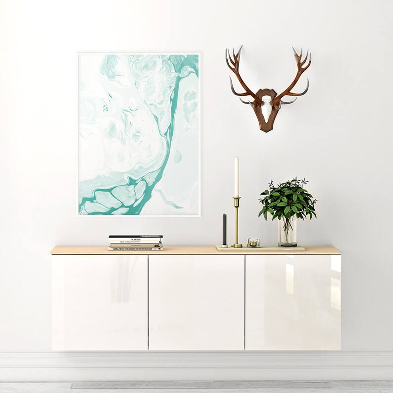 May include: White wall mounted cabinet with three doors. The cabinet has a light wood top and is decorated with a framed abstract painting, a set of antlers, and a potted plant.