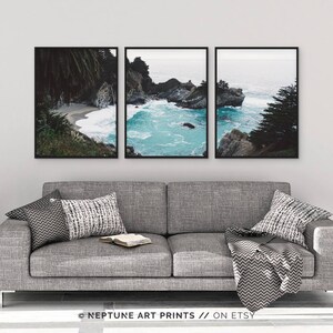 May include: Three framed photographs of a rocky coastline with turquoise water. The photos are arranged in a row on a gray wall above a gray couch with pillows and a throw blanket.