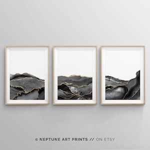 May include: Set of three abstract art prints featuring black and gold agate-like designs. The prints are framed in natural wood frames and have a white background.