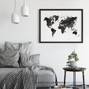 Peut inclure: Une impression de carte du monde en aquarelle noir et blanc dans un cadre noir accroch&eacute; &agrave; un mur blanc au-dessus d'un canap&eacute; gris avec des coussins et une couverture. Le canap&eacute; est dans un salon avec une petite table d'appoint et une plante en pot.