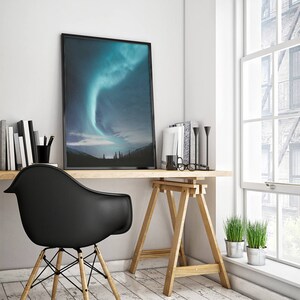 Puede incluir: Una impresi&oacute;n enmarcada en negro de una aurora boreal verde y azul sobre un bosque oscuro. La impresi&oacute;n est&aacute; colgada en una pared blanca sobre un escritorio de madera con una silla negra, un caballete de madera y dos plantas en maceta.