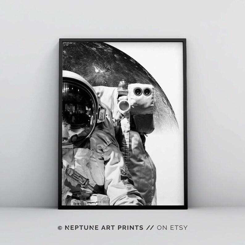 Pode incluir: Fotografia a preto e branco de um astronauta com um fato espacial de p&eacute; em frente &agrave; lua. O capacete do astronauta reflete a superf&iacute;cie da lua. A imagem est&aacute; enquadrada numa moldura preta. &copy; NEPTUNE ART PRINTS // ON ETSY