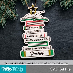 May include: A wooden ornament shaped like a stack of books topped with a star. The books are labeled with the titles The Women, The Alchemist, Harry Potter, The Handmaid's Tale, Killers of the Flower Moon, and the name Rachel in script font.