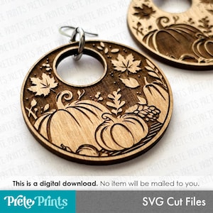 May include: A pair of circular wooden earrings featuring laser-cut designs of pumpkins, maple leaves, and foliage. Each earring has a silver-toned metal hook at the top. The text "This is a digital download. No item will be mailed to you." is visible.