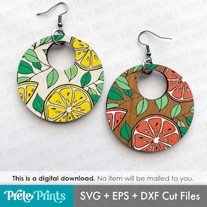 May include: A pair of wooden hoop earrings with fruit designs. One earring features yellow lemons and green leaves on a white background. The other has red grapefruit and green leaves on a wood grain background. The earrings have silver-colored hooks.