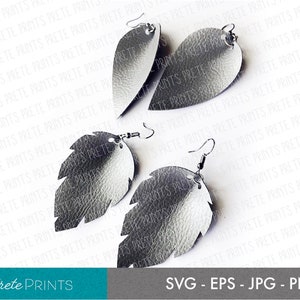 May include: A pair of silver leather earrings shaped like leaves. The earrings have a textured surface and are hanging from silver hooks.