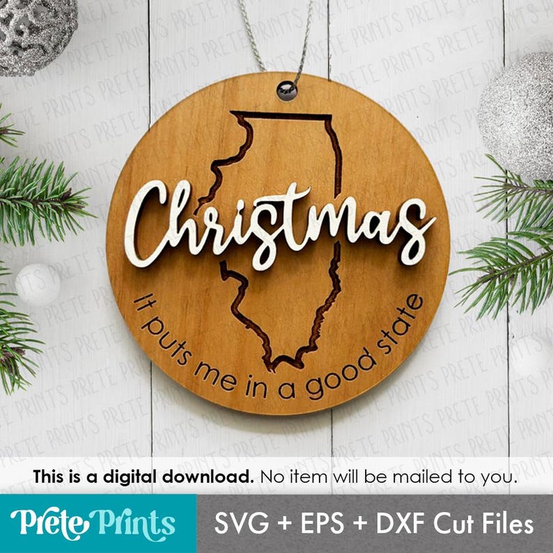 May include: A round wooden Christmas ornament with the state of Illinois cut out. The word "Christmas" is in white script across the top, and the phrase "It puts me in a good state" is along the bottom.