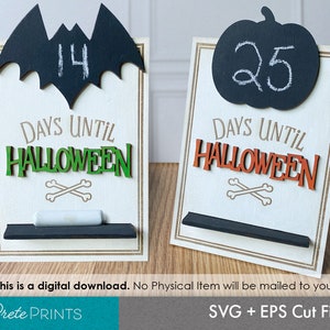 Może przedstawiać: Dwa drewniane znaki odliczające do Halloween z wkładkami z tablicy kredowej. Pierwszy znak przedstawia czarnego nietoperza z numerem 14 i tekstem "DAYS UNTIL HALLOWEEN". Drugi znak przedstawia czarną dynię z numerem 25 i tekstem "DAYS UNTIL HALLOWEEN".