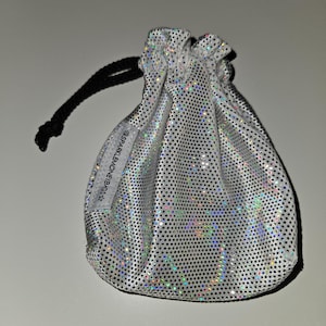 May include: A small, silver drawstring bag with a shimmering, dotted pattern. The bag has a black drawstring closure and a small white tag with text. The bag is made of a shiny, reflective material.
