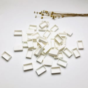 Pode incluir: Um monte de bandejas de tinta de aquarela de plástico branco. As bandejas estão dispostas em um padrão aleatório sobre uma superfície branca.