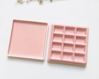 May include: A pink ceramic tray with 16 individual compartments, perfect for organizing small items. The tray is in a square shape and has a smooth, glossy finish.