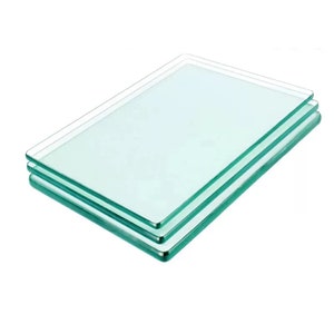 May include: Three clear glass cutting boards stacked on top of each other. The boards have a slightly green tint and rounded edges.