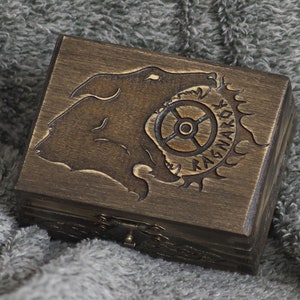 May include: A wooden box with a dark brown stain. The lid is engraved with a wolf's head and a gear with the word "Ragnarok" inscribed on it.