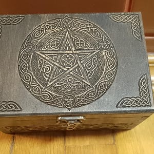 May include: A wooden box with a pentagram design carved into the lid. The box is dark brown and has a metal latch.