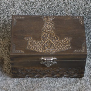 May include: A wooden box with a carved design of a hammer and knotwork. The box has a dark brown finish and a metal latch.
